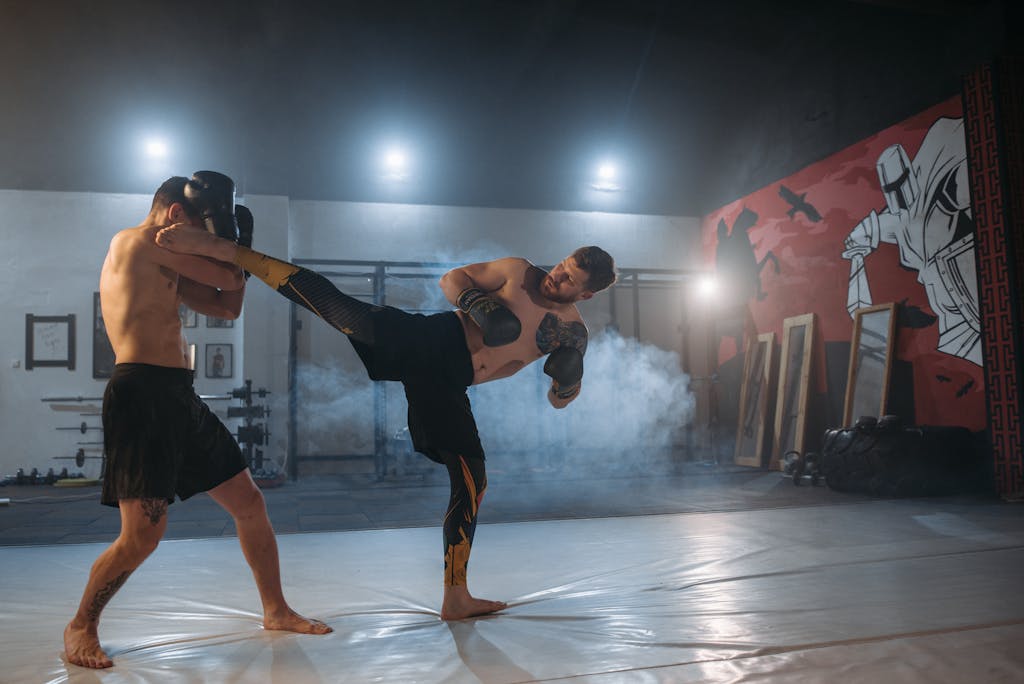 Two male fighters practice kickboxing techniques in a gym, emphasizing strength and agility.
