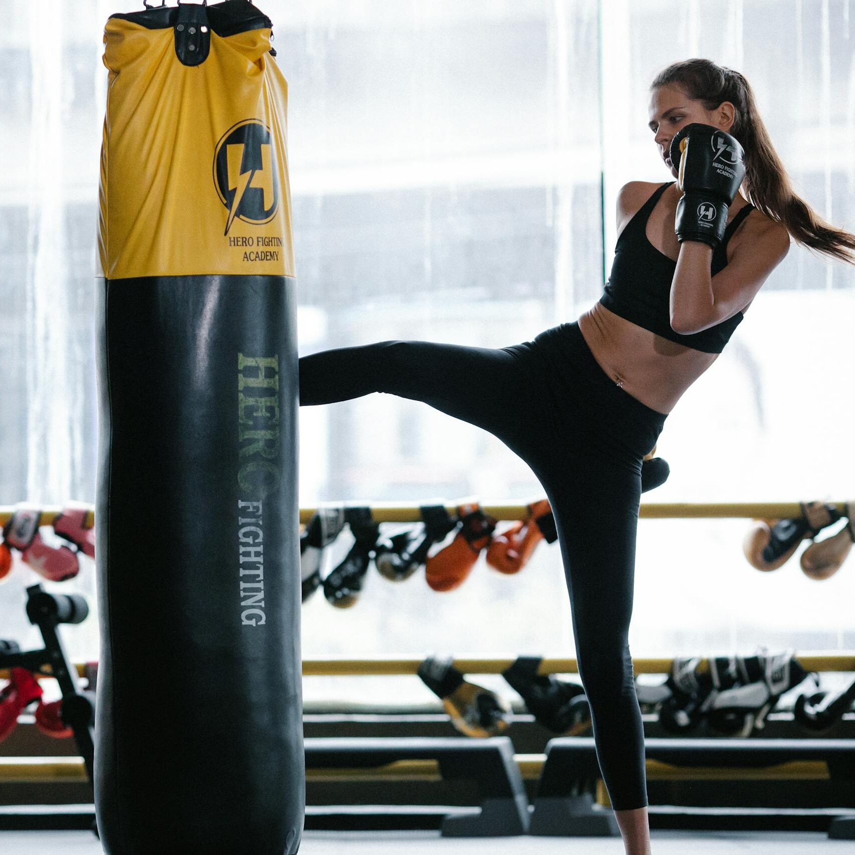 Woman practicing roundhouse kick with boxing coach in a modern gym setting.
